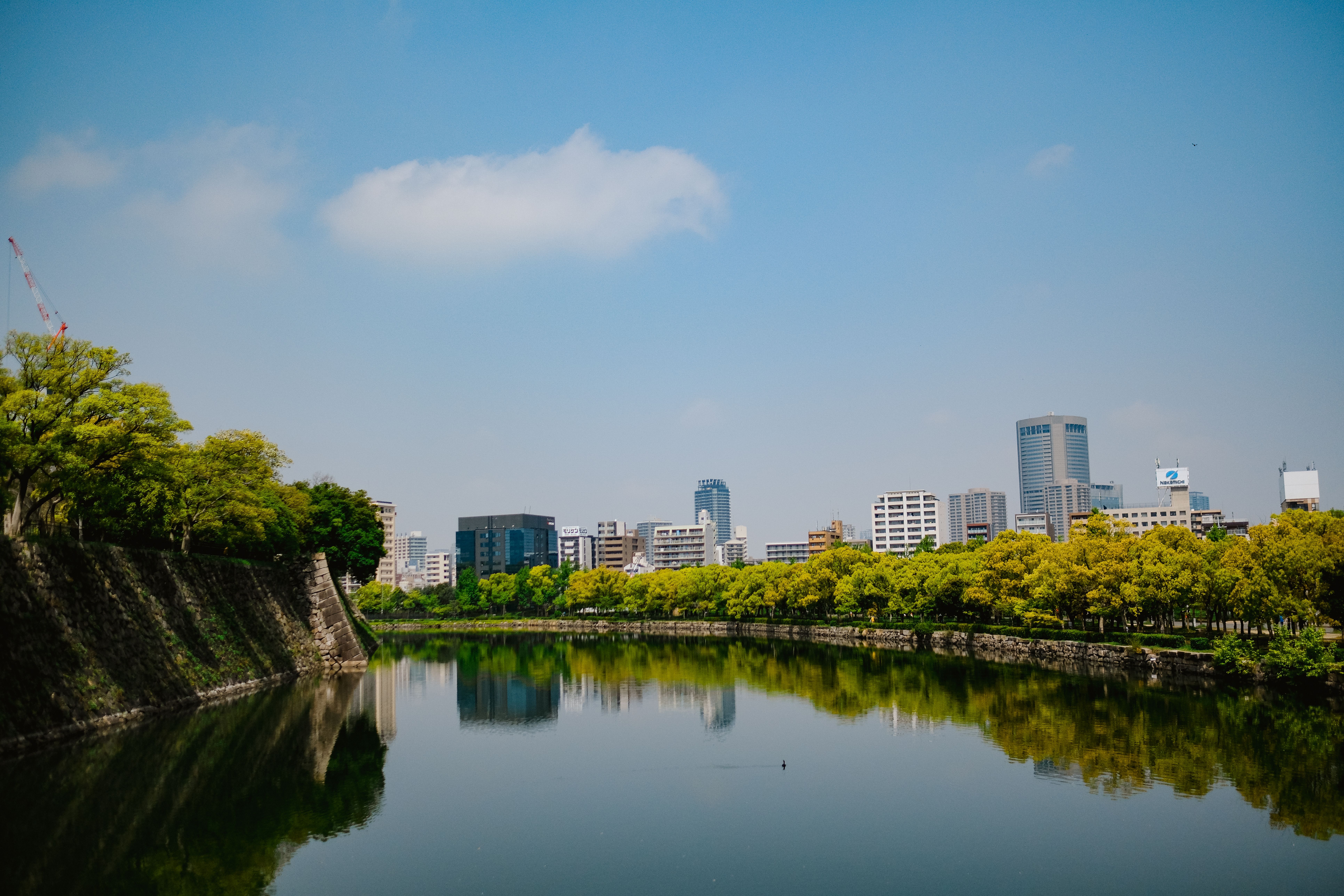 Imperial Palace moat with stone walls and green trees reflecting in the water, Tokyo Marunouchi skyline in the background